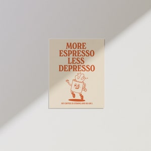 May include: A beige poster with the text "MORE ESPRESSO LESS DEPRESSO" in orange. Below the text is a cartoon coffee cup character with a smiling face. The text "MY COFFEE IS STRONG AND SO AM I." is at the bottom.