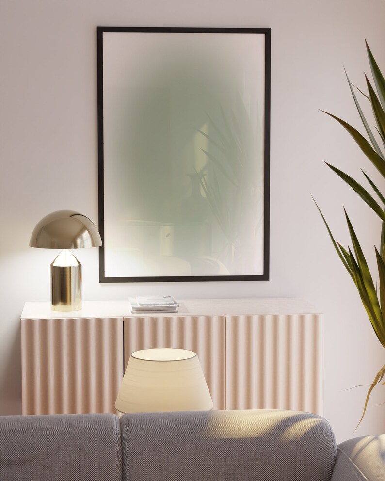 May include: A living room interior with a light beige cabinet with fluted doors, a gold table lamp with a white lampshade, a black framed picture with a green and white abstract design, and a gray couch.