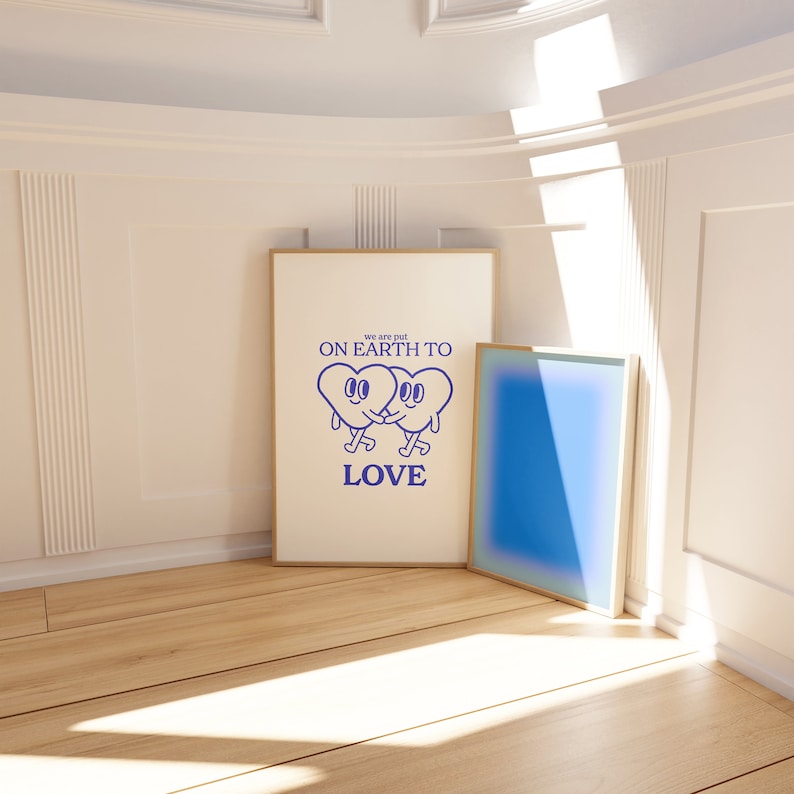May include: Two blue cartoon hearts holding hands with the text "we are put on earth to love" in a white frame on a wooden floor.