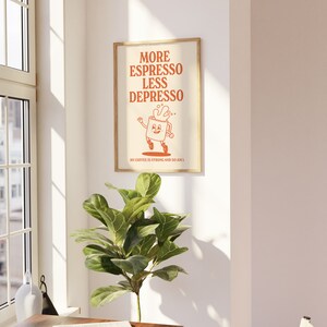 May include: A framed poster with the text "MORE ESPRESSO LESS DEPRESSO" in orange. The poster features a cartoon coffee cup character. The text "MY COFFEE IS STRONG AND SO AM I" is at the bottom. The poster is in a room with a plant.
