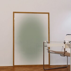 May include: A wooden framed picture with a blurred green background, sitting on a wooden floor next to a white and chrome chair.