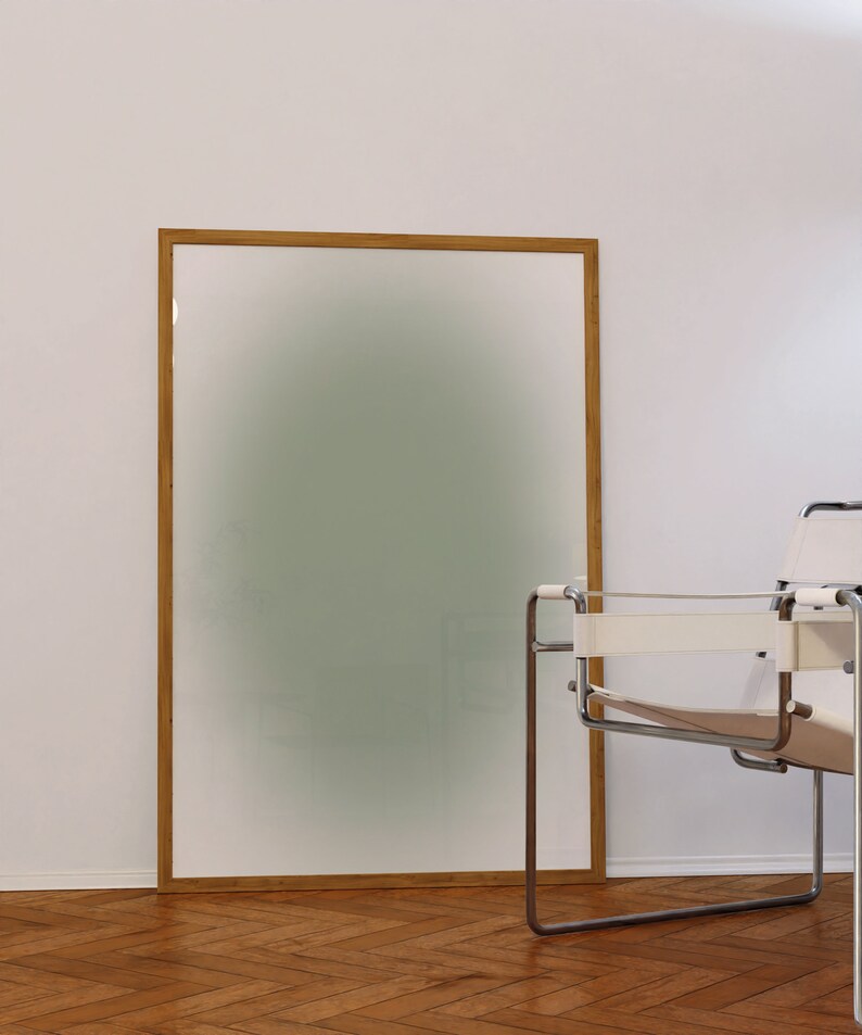 May include: A wooden framed picture with a blurred green background, sitting on a wooden floor next to a white and chrome chair.