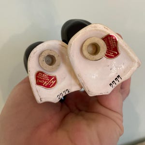 May include: A pair of white ceramic salt and pepper shakers shaped like a couple. The shakers have black painted details and red labels that say "Lady Gay" and "2777".