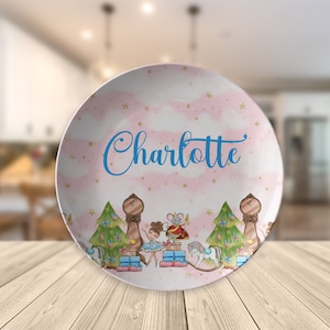 May include: A pink and white personalized plate with a Nutcracker theme. The plate features a ballerina, a mouse king, a nutcracker soldier, and a Christmas tree. The plate is decorated with gold stars and the name "Charlotte" is written in blue cursive.