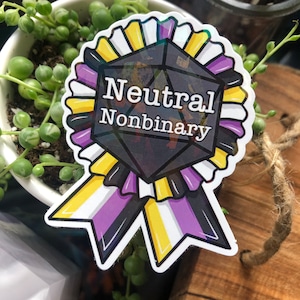 Puede incluir: Una pegatina en blanco y negro con una cinta amarilla, blanca y morada. La pegatina presenta un dado negro de seis caras con el texto "Neutral Nonbinary" en blanco.