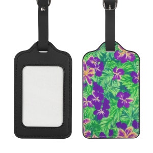 May include: Two luggage tags. One is black with a clear window for an ID. The other tag has a green background with purple and yellow floral pattern. Both tags have a black leather strap and buckle.