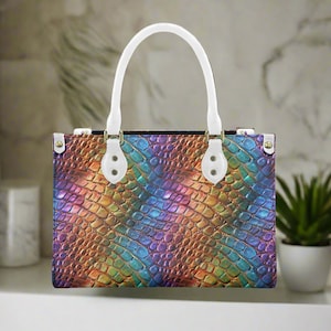 Op de afbeelding: Een regenboogkleurige handtas met een witte leren handvat en gouden accenten. De tas heeft een krokodil-geprägte textuur.