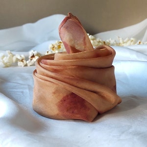May include: A brown silk scarf with a red and orange tie-dye pattern. The scarf is folded into a triangular shape.