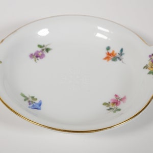 May include: A white porcelain dish with a gold rim and floral designs. The dish has two handles on the sides.