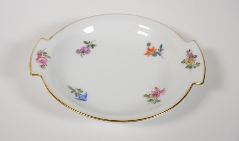 May include: A white porcelain dish with a gold rim and floral designs. The dish has two handles on the sides.