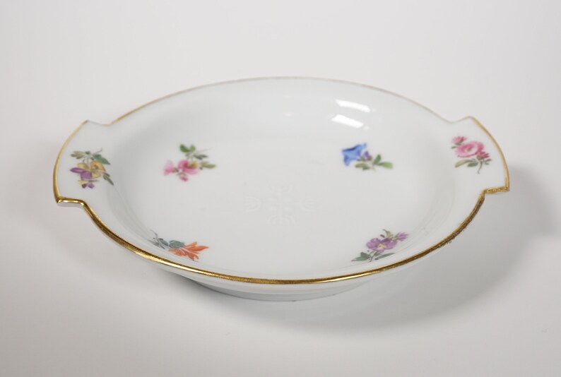 May include: A white porcelain dish with a gold rim and floral designs. The dish has two handles on the sides.