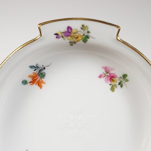 May include: A white porcelain bowl with a gold rim and hand-painted floral designs. The bowl has a scalloped edge and a small handle on each side.