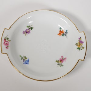 May include: A white porcelain serving dish with a gold rim and floral accents. The dish has two handles and is decorated with hand-painted flowers in shades of pink, purple, blue, yellow, and orange.