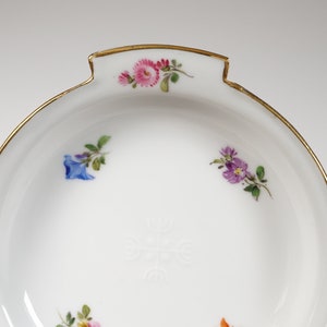 May include: A white porcelain dish with a gold rim and floral decorations. The dish has a scalloped edge and a small handle on one side.