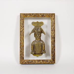 以下が含まれることがあります： 中世の騎士の形をした真鍮製のアンティークドアノッカー。装飾的な金色のフレームに収められています。騎士は詳細なヘルメットと鎧を身に着けています。フレームには華やかな花の模様があります。