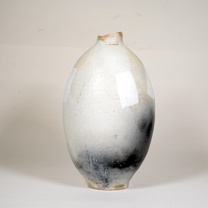 May include: A handcrafted, oval-shaped ceramic vase with a unique color gradient. The vase transitions from white at the top to a dark, smoky black at the base. The top has a slightly irregular opening, adding to its rustic charm.
