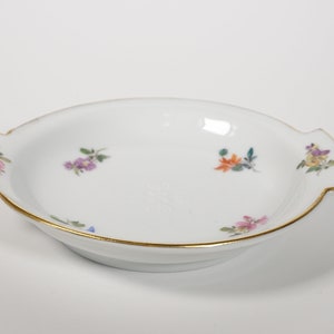 May include: A white porcelain serving dish with two handles and a gold rim. The dish is decorated with small, colorful floral designs.