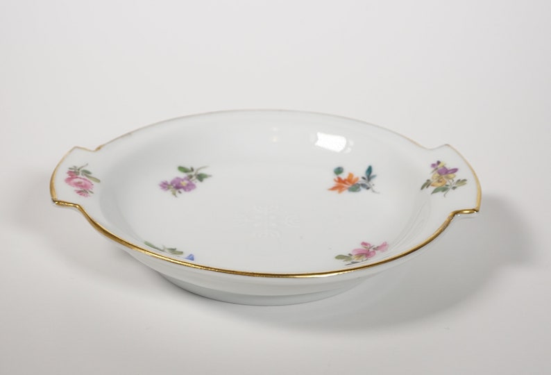 May include: A white porcelain serving dish with two handles and a gold rim. The dish is decorated with small, colorful floral designs.
