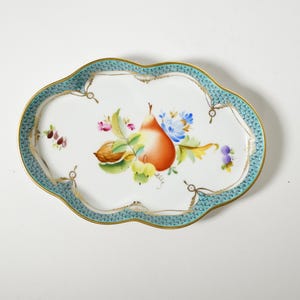 May include: An oval porcelain tray with a scalloped edge featuring a turquoise fish-scale pattern border and a gold rim. The center displays a hand-painted arrangement of a pear, a walnut, and small blue and pink flowers on a white background.