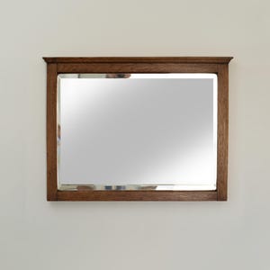 May include: A rectangular wooden framed mirror with a beveled edge. The mirror is hanging on a white wall.