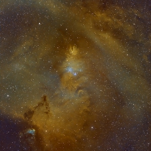 Puede incluir: Un primer plano de una nebulosa en el espacio, con un brillo amarillo-naranja brillante y una nube azul-gris oscura en el centro. La nebulosa está rodeada de un campo de estrellas.