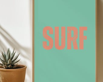 Puede incluir: Una impresión enmarcada con un fondo azul verdoso y la palabra "SURF" en color rosa coral. La impresión está sobre una mesa de mimbre.
