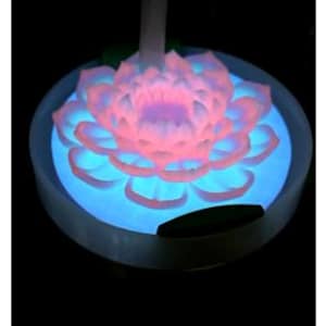 May include: A glowing lotus flower night light. The flower petals are pink and white, with a blue glow emanating from the base. The light sits in a white circular base, creating a serene and calming ambiance.