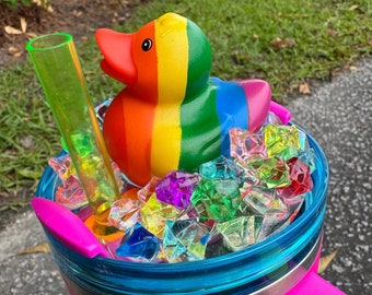 May include: A pink stainless steel tumbler with a blue lid and a rainbow rubber ducky inside. The tumbler is filled with colorful plastic gems.
