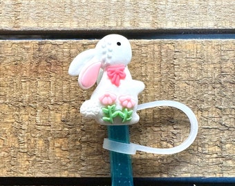May include: White bunny pencil topper with pink flowers and a pink bow. The bunny is attached to a blue pencil with a clear plastic ring.
