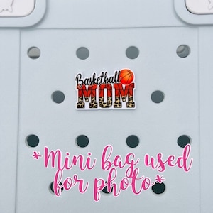 May include: A small, white, round, plastic bag with a black and orange basketball design with the words "Basketball Mom" and a basketball graphic. The bag is on a light blue background with a pink text overlay that says "*mini bag used for photo*"