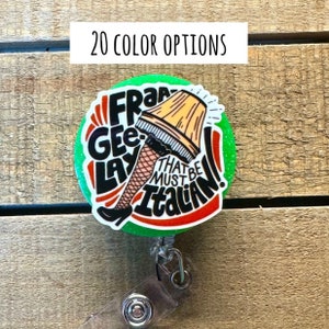May include: A green, red, and white badge reel with a cartoon image of a woman's leg wearing a fishnet stocking and a lampshade on her head. The text on the badge reel reads "Fra Gee Lay That Must Be Italian!"