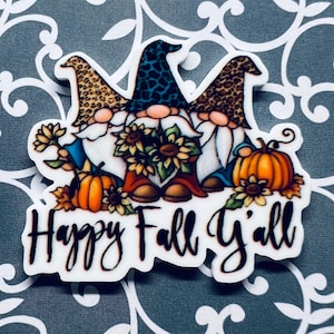 May include: Three gnomes with leopard print hats and beards, holding sunflowers and pumpkins. The gnomes are standing on a white background with the text "Happy Fall Y'all".