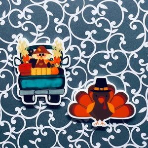 May include: Two Thanksgiving themed stickers. One sticker features a blue pickup truck with a scarecrow and pumpkins in the bed. The other sticker features a brown turkey wearing a pilgrim hat.