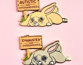Può includere: Due spille in smalto dorato con un coniglio dei cartoni animati con gli occhi pieni di lacrime. La prima spilla ha un cartello che dice "Autistico e sopraffatto". La seconda spilla ha un cartello che dice "Esausto e sopraffatto".