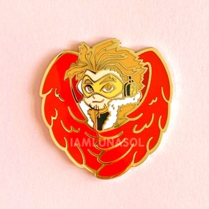 May include: Gold-colored enamel pin featuring a cartoon character with yellow hair, a yellow mask, and red wings. The character is wearing a white collar and a black jacket. The text "IAMLUNASOL" is visible on the pin.