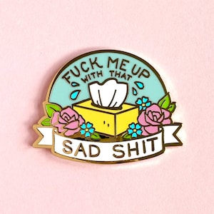 May include: Gold enamel pin with a blue background and the text "Fuck me up with that sad shit". The pin features a yellow tissue box with a white tissue and pink flowers.