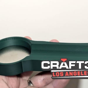 May include: A dark green 3D-printed object with a circular opening and a rectangular extension. The text "CRAFT3D LOS ANGELES" is printed on the object in white and red.