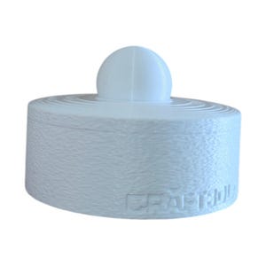 May include: A white, cylindrical object with a rounded top and a smaller, spherical element on top. The object has a textured surface and the word "CRAFTED" is visible on the side. The item is likely a decorative or functional piece.