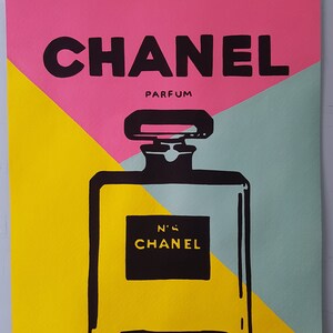 May include: A black and white illustration of a Chanel perfume bottle on a yellow, pink and blue background. The text "CHANEL PARFUM" and "N&deg;5 CHANEL" are visible. The image is signed "Andy Warhol".