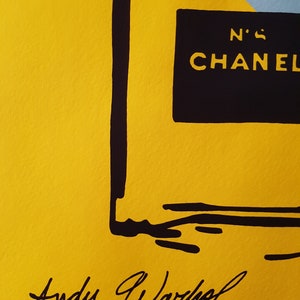 May include: A yellow background with a black outline of a perfume bottle. The bottle has a black label with the text "N'5 CHANEL" on it. The image is signed "Andy Warhol" in black ink.