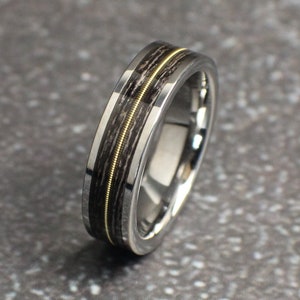 May include: A silver and black tungsten carbide ring with a thin gold inlay. The ring has a brushed finish.