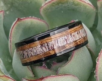May include: A black and brown ring with a wood inlay design. The ring is sitting on a green succulent plant.