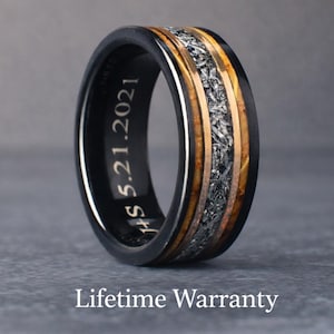 May include: A black ring with a central band of silver and gold-toned metal. The ring has a black outer band with the inscription "HS 5.21.2021". The ring is a unique piece of jewellery.