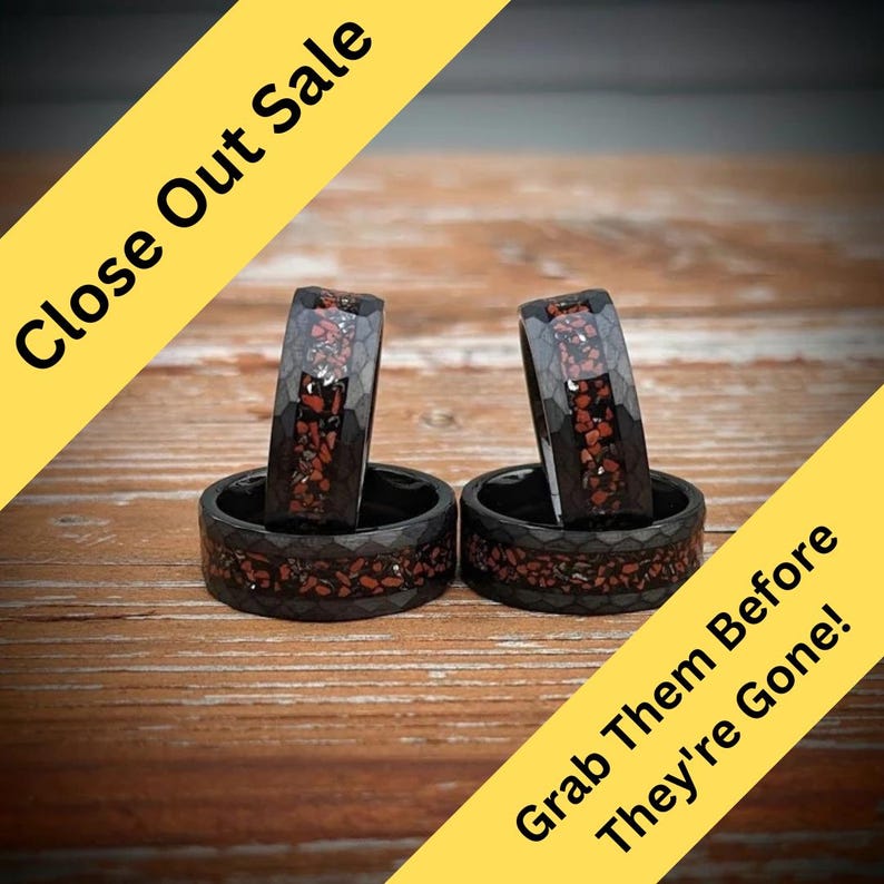 May include: Four black rings with red and silver flecks. The rings are stacked on a wooden surface. The text "Close Out Sale" and "Grab Them Before They're Gone!" is visible in the image.