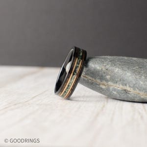 May include: A black tungsten carbide ring with a wood inlay. The inlay features green and brown wood with a black line separating the two colours.