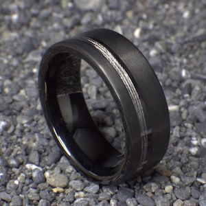 May include: A black tungsten carbide ring with a silver cable inlay. The ring has a brushed finish.