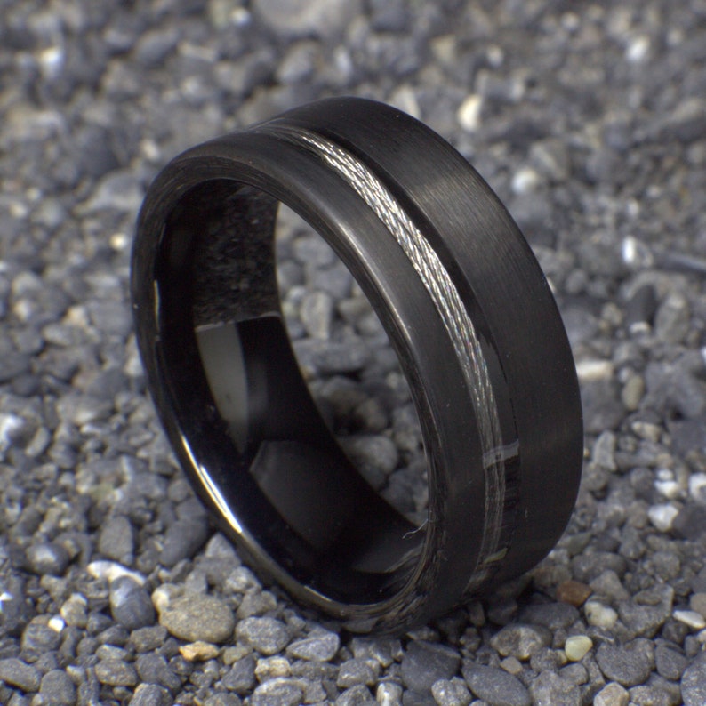 May include: A black tungsten carbide ring with a silver cable inlay. The ring has a brushed finish.