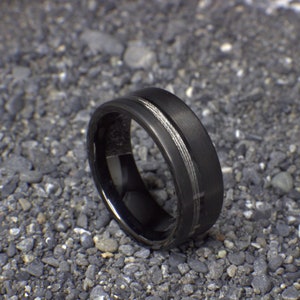 May include: A black tungsten carbide ring with a silver inlay. The ring has a brushed finish and a beveled edge.