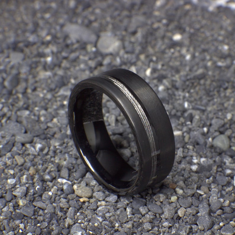 May include: A black tungsten carbide ring with a silver inlay. The ring has a brushed finish and a beveled edge.
