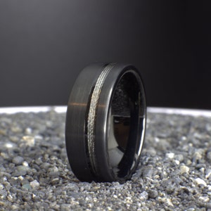 May include: A black tungsten carbide ring with a silver inlay. The ring has a brushed finish and a polished edge.